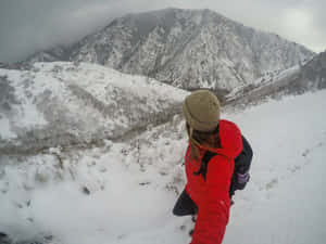 穿著紅色外套和毛帽的登山者穿越白雪覆蓋的山谷。 — 冬季風景 壁紙