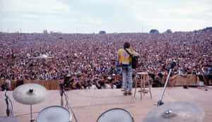 一位音樂家在戶外音樂會上為大批人群在舞台上表演。 — Woodstock 壁紙