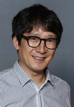 一位戴眼鏡、穿條紋襯衫的男士在工作室肖像中微笑。 — 凱羅·忍 壁紙