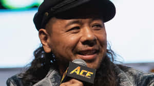 長髮戴帽男子微笑著手持ACE麥克風。 — WWE GIF 壁紙