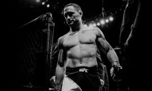一位身穿UFC短褲、有刺青的MMA拳手，在明亮的燈光下於八角籠內行走。 — 終極格鬥冠軍賽 壁紙