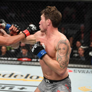 UFC拳手在八角籠內揮拳，背景有觀眾。 — 運動 壁紙
