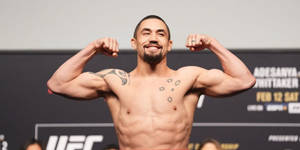 UFC拳手在稱重活動中彎曲手臂，展示刺青胸膛和微笑面容。 — 運動 壁紙