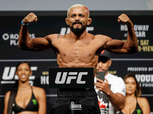 UFC拳手在體重磅上彎曲手臂，身後有兩名女性。 — 終極格鬥冠軍賽 壁紙