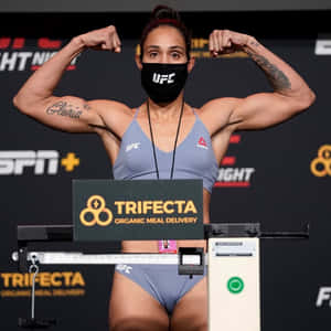 女UFC拳手在稱重時彎曲手臂，戴著口罩和灰色裝備。 — 運動 壁紙