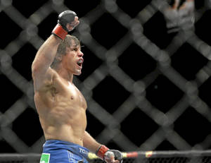 一位赤裸上身的MMA戰士在八角籠內高舉拳頭慶祝勝利。 — 運動 壁紙
