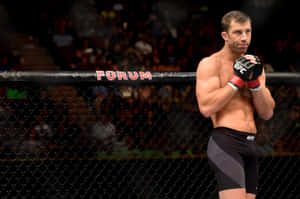 一位赤裸上身的 MMA 戰士穿著黑色短褲和手套，站在帶有 'FORUM' 標誌的 UFC 八角籠內。 — 終極格鬥冠軍賽 壁紙