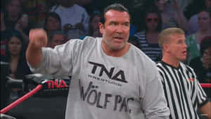 摔角手穿著灰色 TNA Wolf Pac T恤，在裁判附近於擂台上揮拳。 — WWE GIF 壁紙