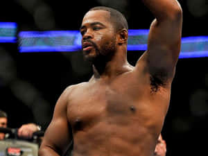 一位赤裸上身的MMA鬥士在明亮的八角籠中勝利地舉起手臂。 — 終極格鬥冠軍賽 壁紙