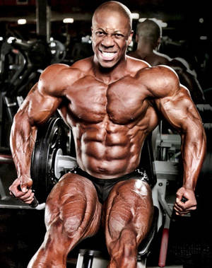 一位赤膊的肌肉男在健身房繃緊，展現清晰的腹肌和手臂。 — 弗萊克斯·惠勒 壁紙