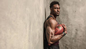 運動型黑人男子靠著混凝土牆手持橄欖球。 — Dk Metcalf 壁紙