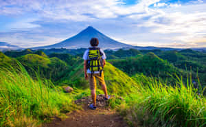 背著綠色背包的健行者欣賞日出時的火山。 — 山脈 壁紙