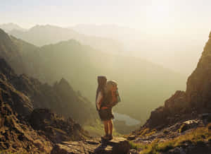 背著背包的登山者站在山脊上，日出時俯瞰山谷 — 登山 壁紙