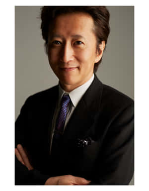 一位微笑的男士身穿黑色西裝和圖案領帶，雙臂交叉。 — 阿基拉 壁紙