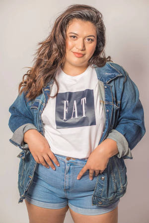 一位穿著牛仔外套和短褲的女性，微笑著穿著印有「FAT」字樣的T恤。 — 模特兒 壁紙