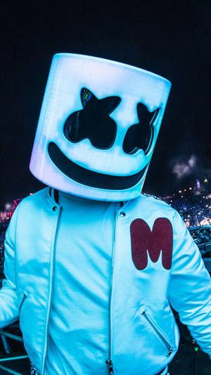 DJ Marshmello 在夜間音樂會中戴著發光頭盔，身後有人群。 — Marshmello iPhone 壁紙