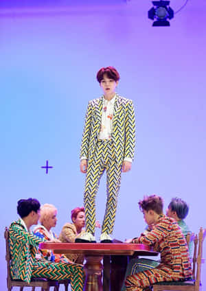 K-pop 表演者穿著圖案西裝在舞台上，其中一人站在桌子上。 — BTS V 動圖 壁紙