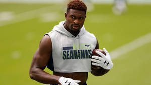 西雅圖海鷹隊美式足球員在草地上抱著一個球。 — Dk Metcalf 壁紙