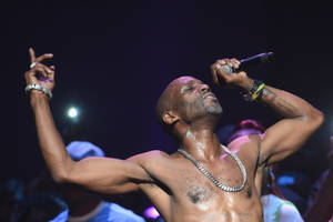 赤裸上身的男歌手在舞台上高舉雙臂和麥克風表演 — DMX 壁紙