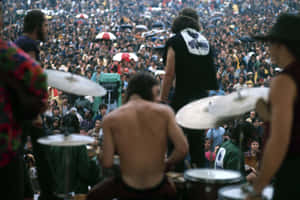 赤裸上身的鼓手在雨中戶外音樂會上表演，大量群眾撐著傘。 — Woodstock 壁紙