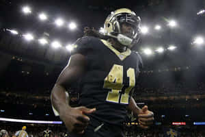 身穿聖徒隊制服的美式足球員在夜間比賽中豎起大拇指。 — Alvin Kamara 壁紙
