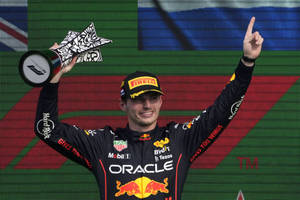 F1車手在頒獎台上手持獎盃慶祝勝利，並指向天空。