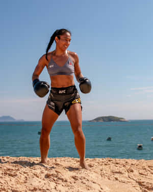 身穿UFC裝備的女性MMA拳手在陽光海灘上微笑，背景有海洋和島嶼。 — 海灘 壁紙