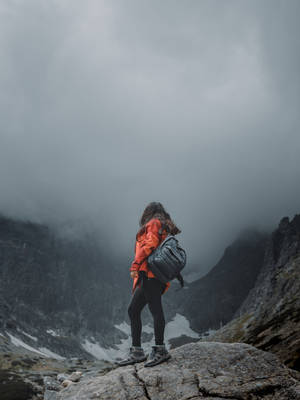 身穿橙色外套的人站在岩石山頂上，下方是霧氣瀰漫的山谷。 — 獨自一人 壁紙