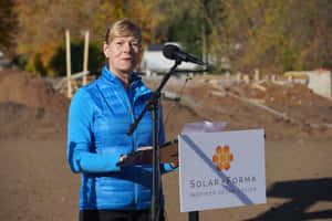 藍色外套女性在建築工地講台發言，帶有Solar Forma標誌。 — 選舉 壁紙