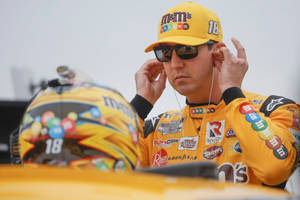 身穿黃色M&M's制服的NASCAR車手在頭盔附近調整耳機。 — 運動 壁紙