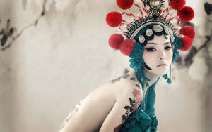 身穿華麗中國戲曲服飾、帶有紅色絨球和青綠色花卉紋身的女人。 — 模特兒 壁紙