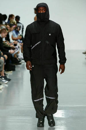 模特兒身穿全黑街頭服飾，戴著連帽和口罩走伸展台。 — Skepta 壁紙