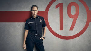 身穿制服的女消防員站在有紅色數字19的牆前。 — 19號消防站 壁紙