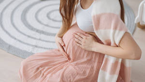 孕婦在家中的螺旋形地毯上坐著，輕輕抱著肚子。 — 懷孕 壁紙