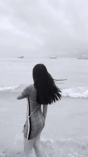 身穿格子裙的女性站在海邊，背景有波浪和船隻，霧氣朦朧。 — 海灘 壁紙