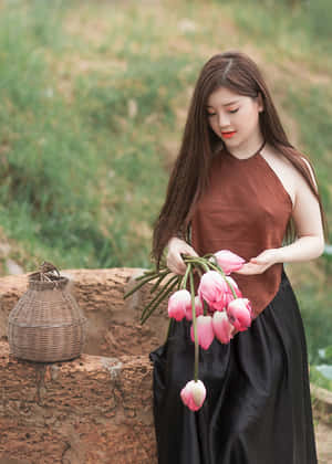 女子在石牆上的柳條籃旁邊拿著粉紅色的鬱金香。 — 高畫質月亮 壁紙