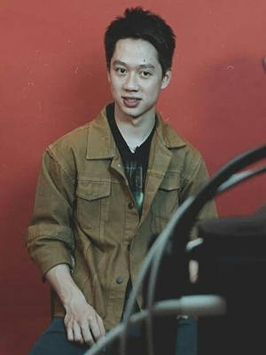 年輕男子身穿棕色外套在紅牆前微笑 — 羽球 壁紙