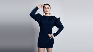 身穿海軍藍連衣裙的女性在灰色背景下擺姿勢，手放在臀部和額頭附近。 — 喬伊·金 壁紙