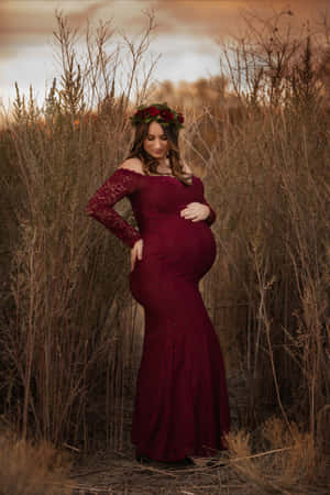 身穿紅色蕾絲裙、頭戴花環的孕婦站在夕陽下的金色草叢中。 — 懷孕 壁紙