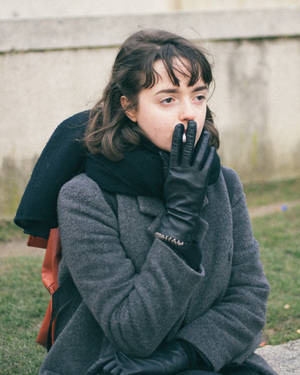 年輕女性穿著冬季外套和手套，在戶外混凝土牆附近手持香煙。 — 抽菸 壁紙
