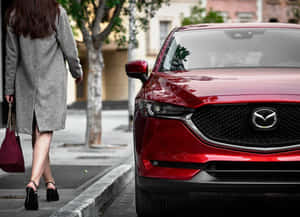 身穿灰色外套的女性在城市人行道上走過紅色Mazda SUV。 — 馬自達 壁紙