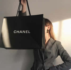 身穿灰色西裝外套的女性在陽光充足的房間裡將大型黑色Chanel手袋舉過臉部。 — 香奈兒 壁紙