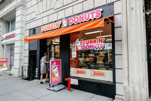 一位女士在城市街道上走過一間有橙色遮陽篷的Dunkin' Donuts店鋪。