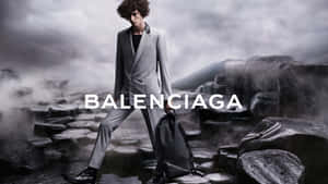身穿灰色西裝的模特兒在霧氣瀰漫的岩石上行走，帶有 Balenciaga 標誌。 — 巴黎世家 壁紙