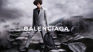 身穿灰色西裝的模特兒在霧氣岩石上行走，帶有Balenciaga標誌。 — 巴黎世家 壁紙