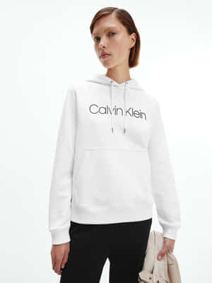 身穿白色Calvin Klein連帽衫和黑色褲子，手持米色手提包的女性。 — 卡文克萊 壁紙