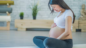 孕婦盤腿坐在瑜伽墊上，在寧靜的工作室中抱著肚子。 — 懷孕 壁紙