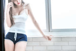 身穿白色上衣和海軍藍短褲的女性靠在一扇明亮的窗戶旁。 — 模特兒 壁紙