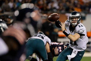 NFL四分衛在夜間比賽中擲出橄欖球，背景人群模糊。 — 美式足球 壁紙