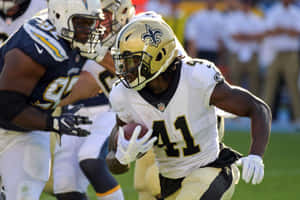 身穿聖徒隊球衣的美式足球員在比賽中帶球奔跑。 — Alvin Kamara 壁紙